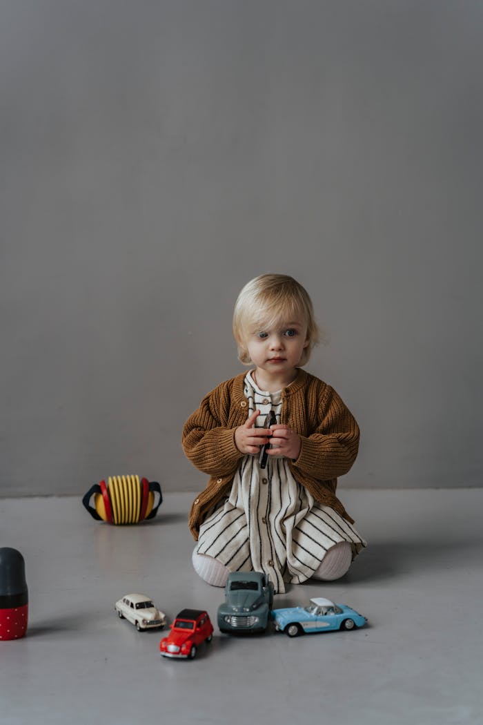 About Adorable child sitting on the floor playing with colorful toy cars indoors.